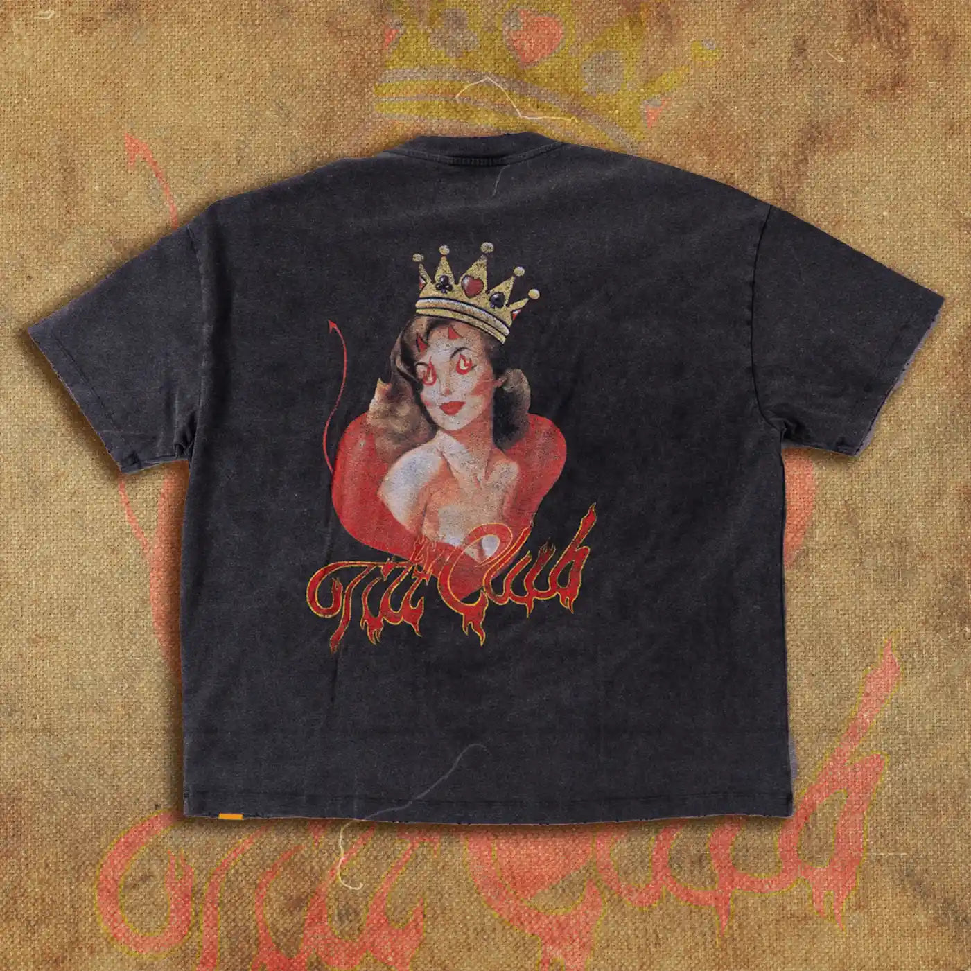 Back view of a black t-shirt featuring a large graphic of a crowned devil girl with red flames and the Tilt Club logo in fiery script, displayed on a textured, flame-inspired backdrop.