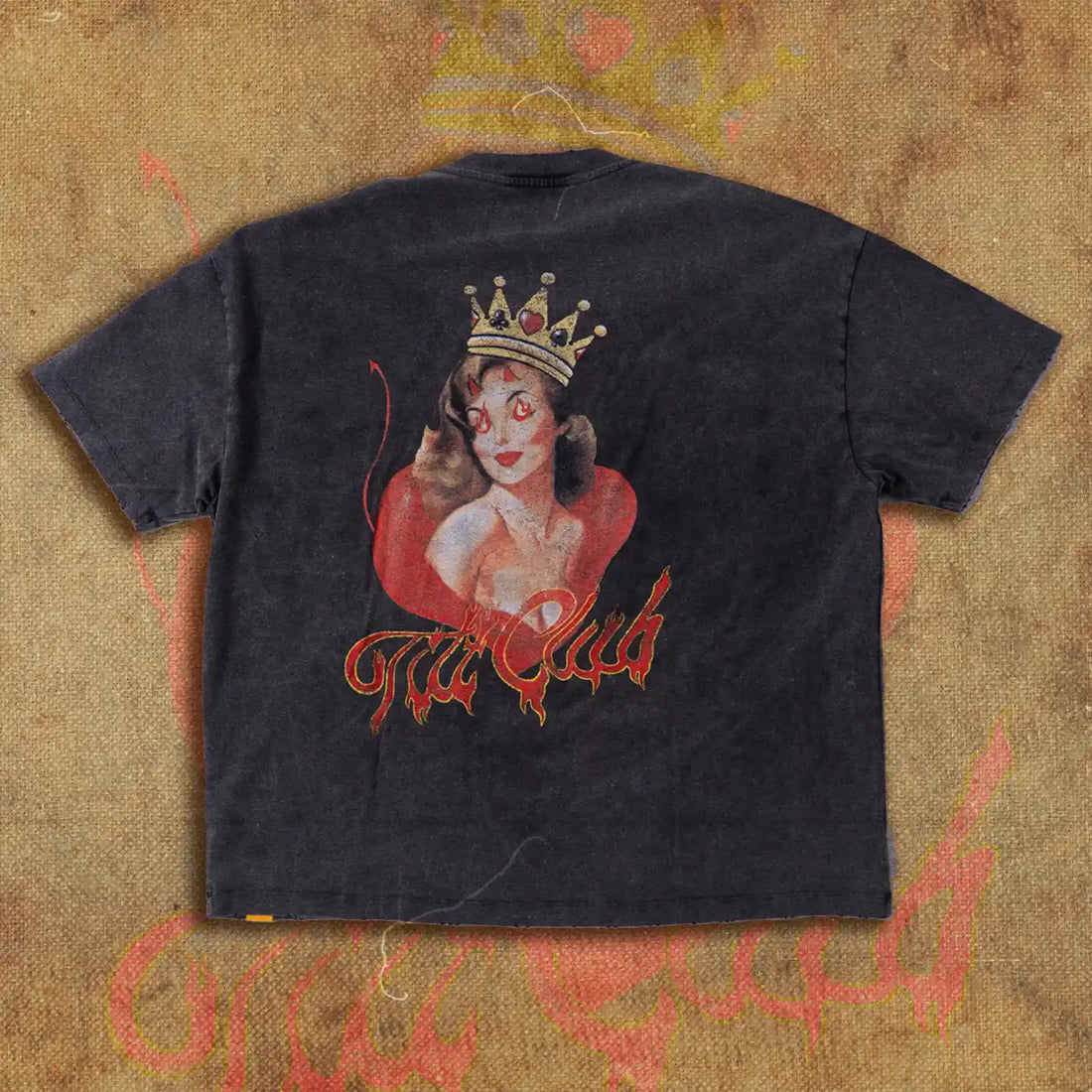 Back view of a black t-shirt featuring a large graphic of a crowned devil girl with red flames and the Tilt Club logo in fiery script, displayed on a textured, flame-inspired backdrop.